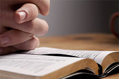Picture of a persons hands folded over a bible